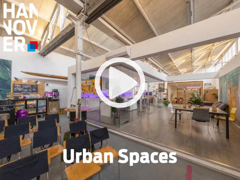 Moderner Co-Working-Space mit Glasbüros, Lounge-Bereich, Café und industriellem Design unter heller Dachkonstruktion.